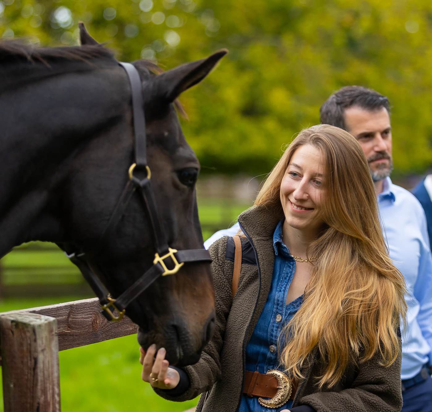 Alexia Ghem caressant le museau d'un cheval dans un pré, accompagnée d'un collègue